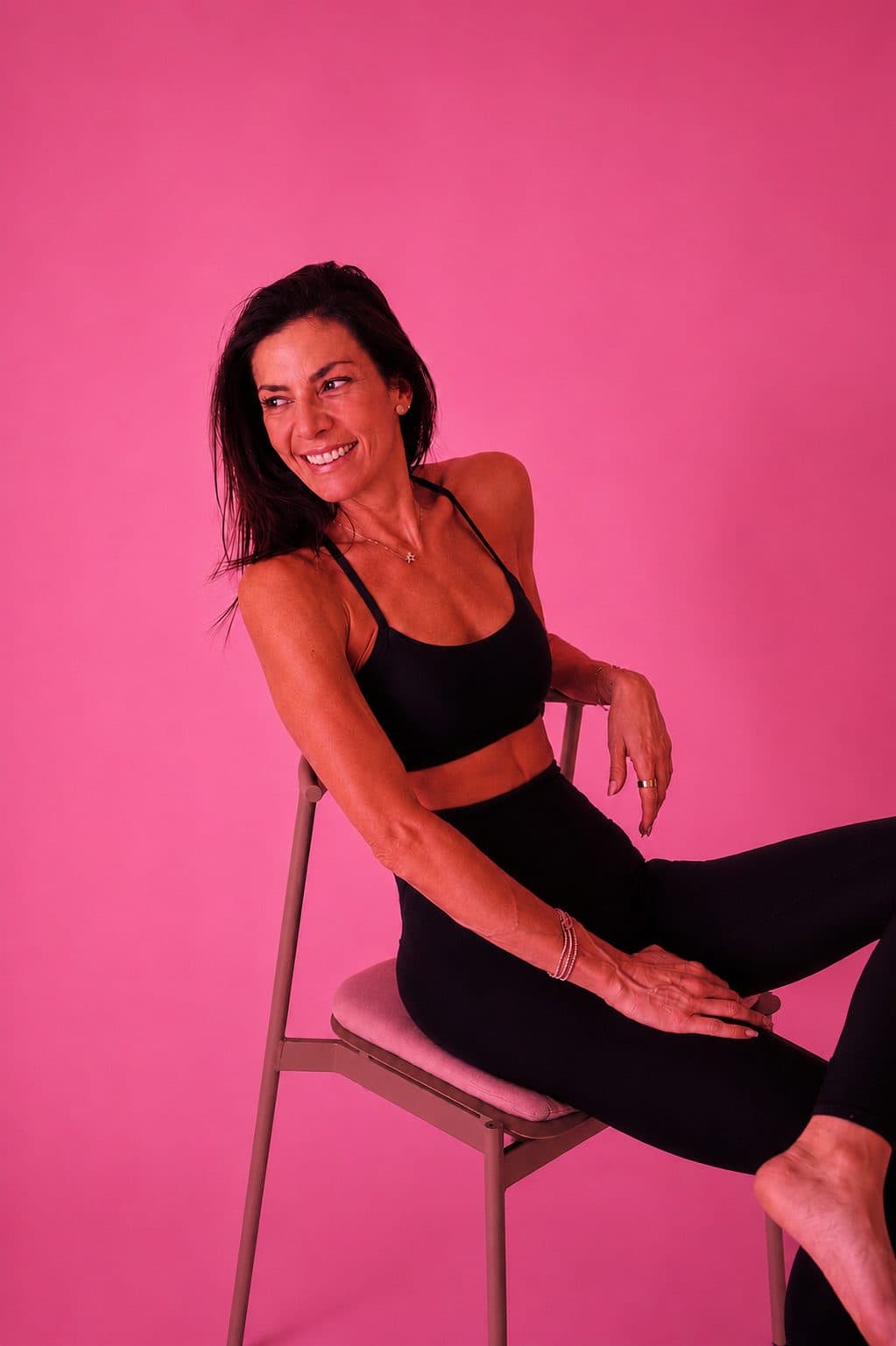 Retrato sonriendo, sentada en una silla sobre fondo rosa